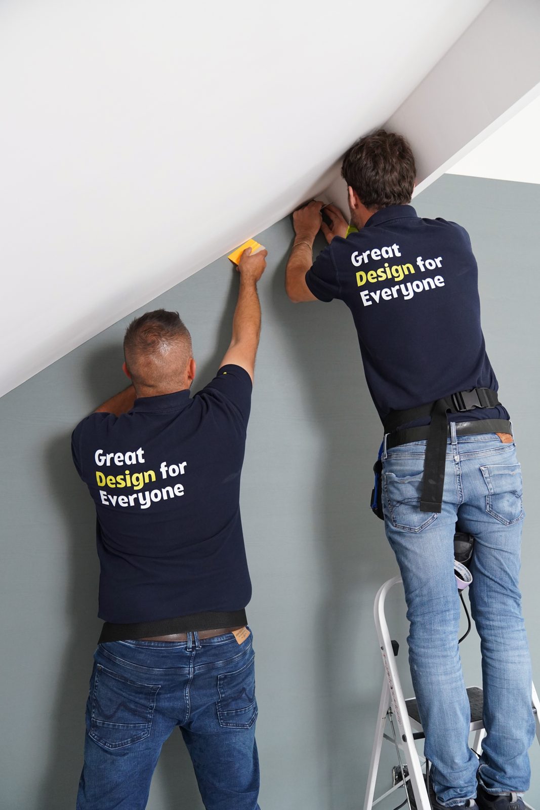 Dos instaladores terminando un muro gris bajo una escalera